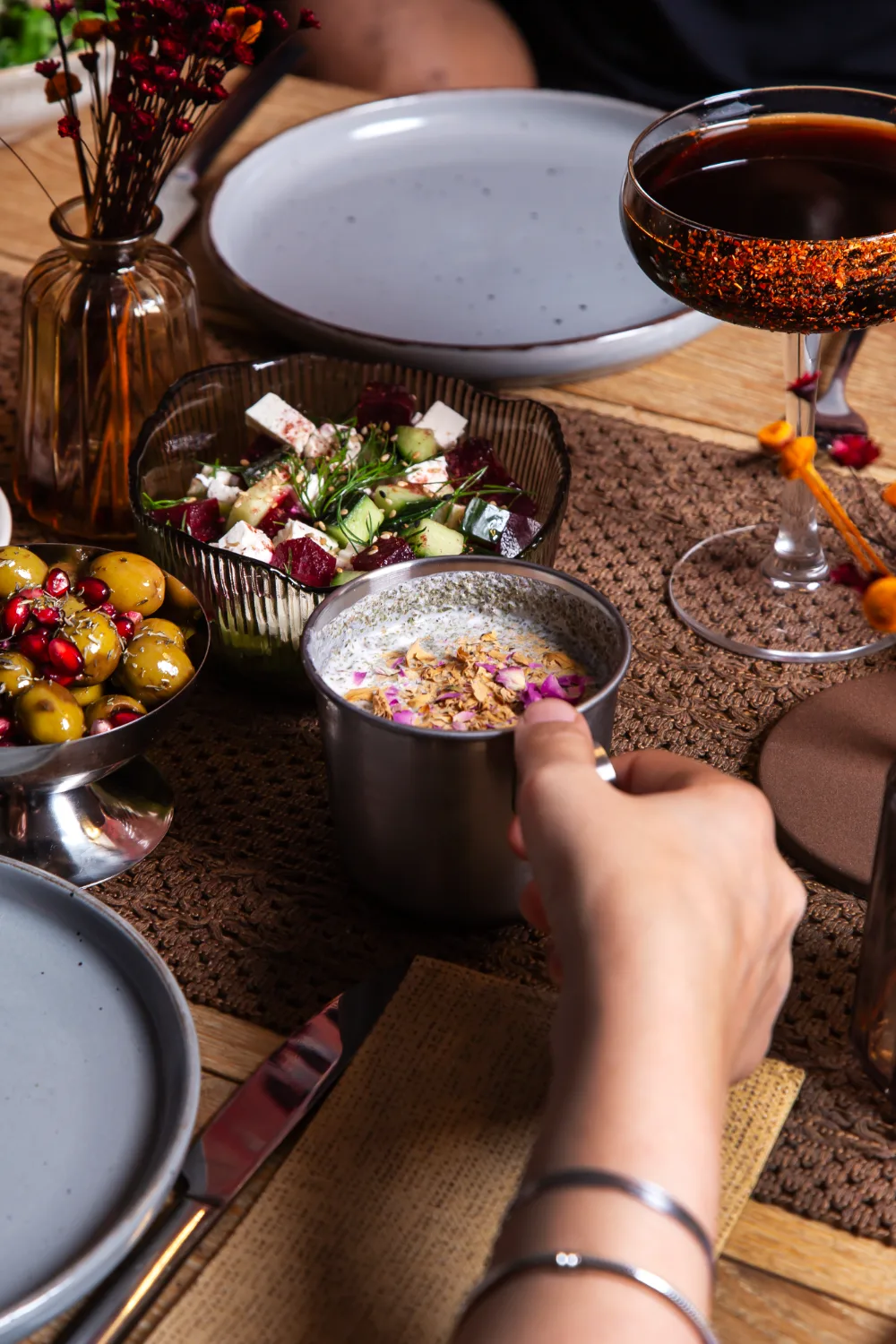 Entrantes persas: ensalada de remolacha y feta, mast-o-khiar con pétalos de rosa y aceitunas con granada, junto a una copa de bebida, en Pérsico restaurante persa Madrid